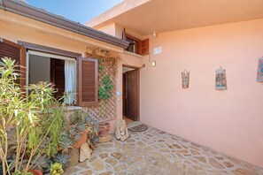 A stone-paved courtyard with a wooden door, a window with shutters, and a wall with a sign and two framed artworks. - Holiday Home 'Villetta Cala Paradiso' with Sea View, Shared Terrace and Air Conditioning (Salina Bamba)
