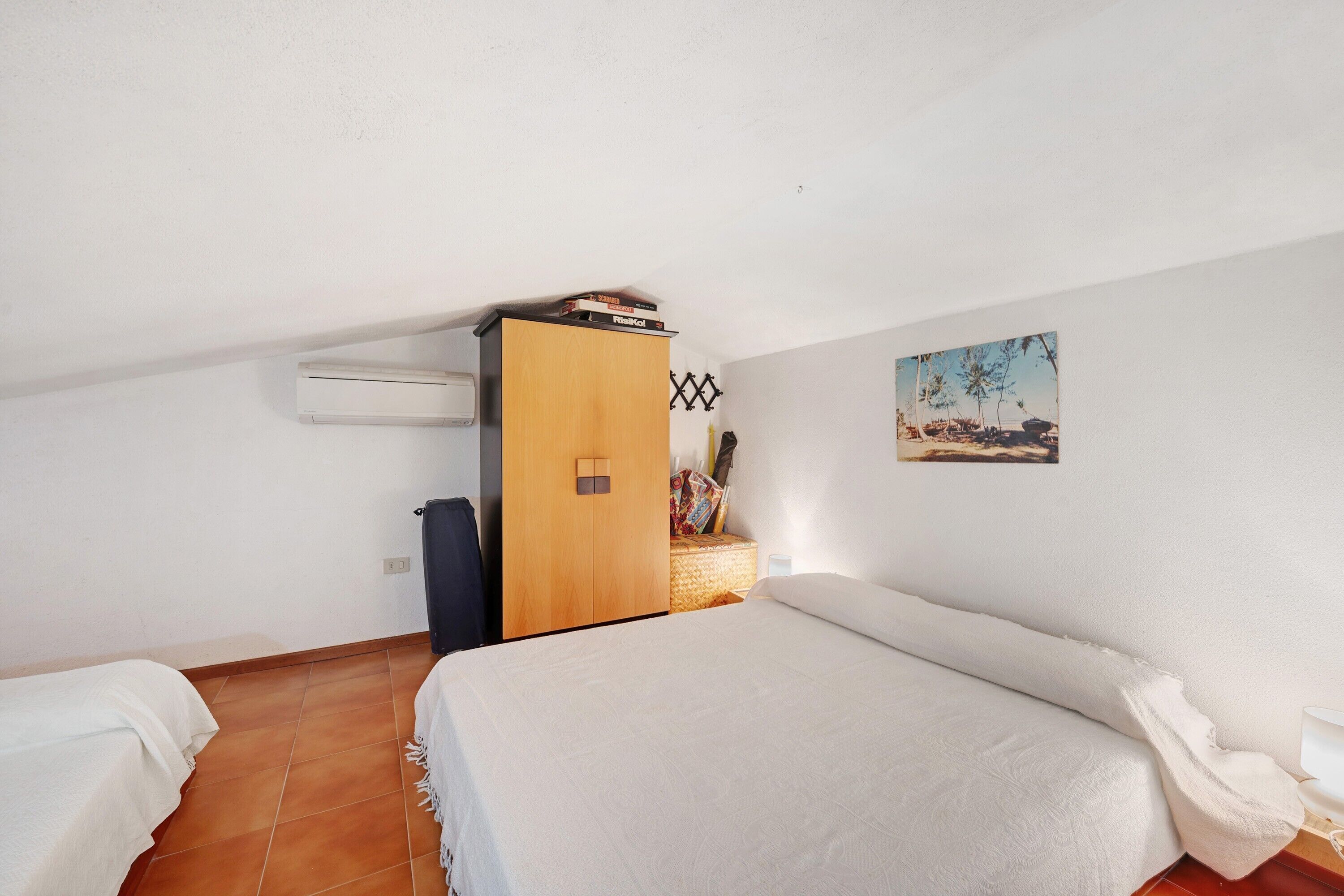 Un dormitorio con cama, armario, aire acondicionado y un cuadro de una escena de playa en la pared.