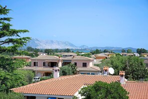 A coastal village with traditional Mediterranean architecture, terracotta roofs, and a backdrop of mountains.