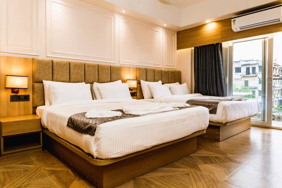 A hotel room with two beds, a wooden headboard, a nightstand, and a large window with a view of buildings.