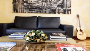 Un salon avec un canapé, une table basse sur laquelle sont posés des livres et un arrangement floral, et une guitare appuyée contre le mur.