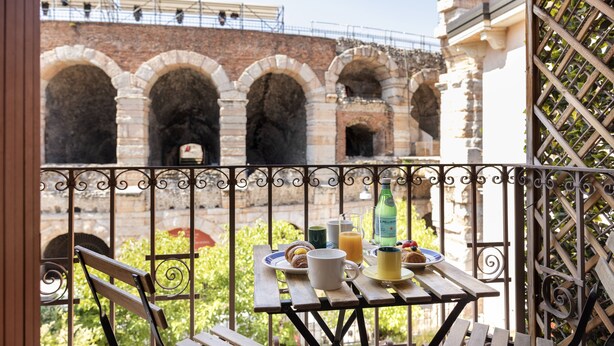Un balcon avec une table dressée pour le petit-déjeuner, un mur en briques et une balustrade en fer forgé.