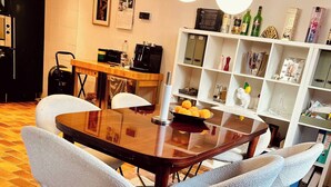 Un coin repas comprenant une table ronde, quatre chaises, une machine à café et une étagère contenant divers objets.