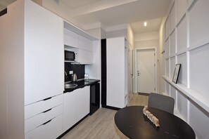 Et moderne køkken med hvide skabe, en sort bordplade og en mikrobølgeovn. I forgrunden står et lille bord med en stol.