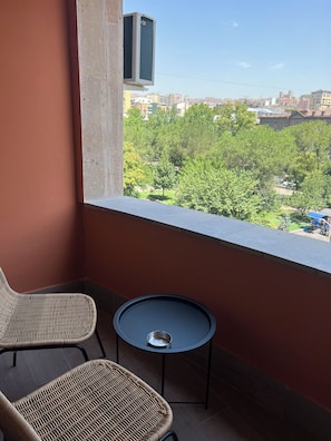 A balcony with wicker chairs, a small round table, and a view of a cityscape with buildings and trees. - Modern studio apartment in the city centre (Yerevan)