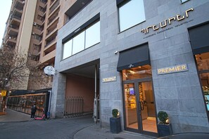 Een hotelingang met een 'Premier' bord, een glazen deur en een kleine potplant erbuiten.