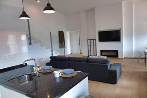 Ett modernt kök med en integrerad köksö, en matplats med soffa och ett vardagsrum med tv.