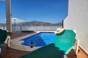 Ein Poolbereich mit Bergblick, ein Stuhl, eine Weinflasche und ein Sonnenschirm.