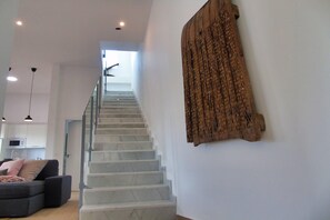 Eine Treppe führt zu einer Empore mit modernem Interieur, darunter ein graues Sofa und Pendelleuchten.