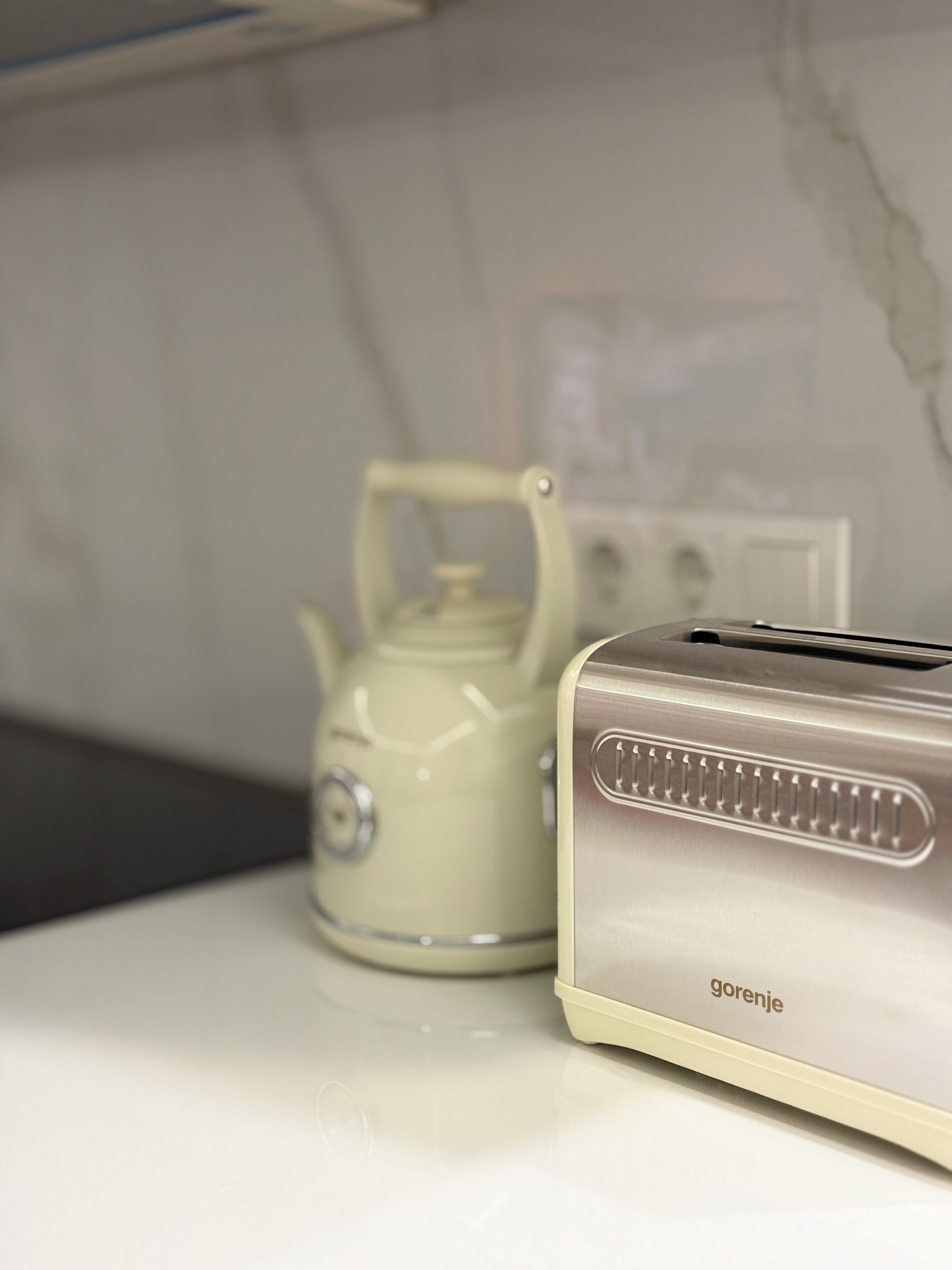 A kitchen with a white countertop, a beige kettle, and a silver toaster with the brand name 'gorenje'.