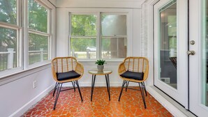Een serre met twee rieten stoelen, een bijzettafeltje met een plant, en uitzicht op de omgeving.