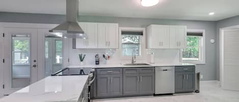A modern kitchen with white cabinets, a large island, and a stainless steel range hood.