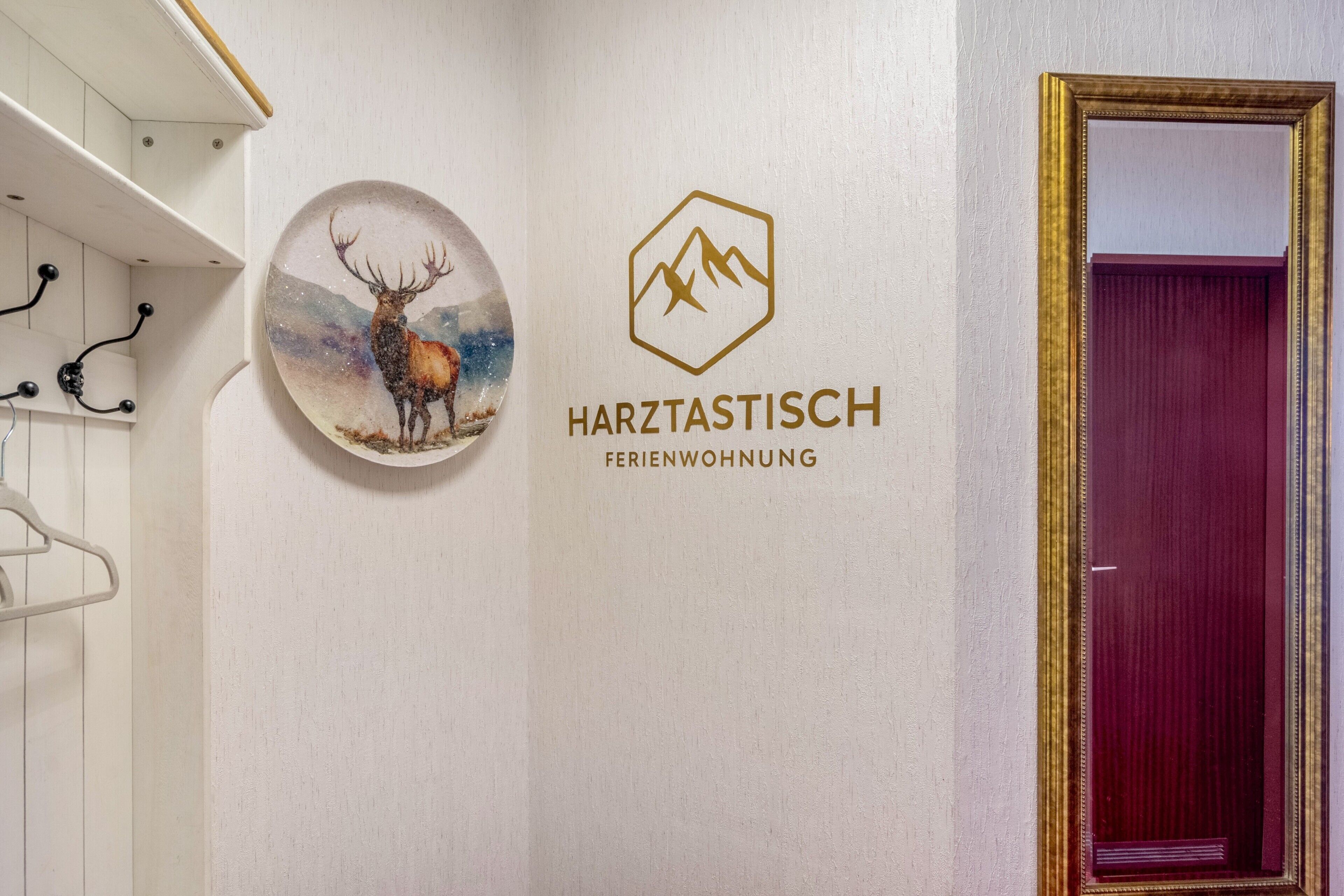 Un mur orné d’une œuvre d’art circulaire représentant un cerf, d’un logo avec une montagne et une étoile, et de l’inscription « HARZTASTISCH FERIENWOHNUNG ».