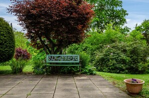 A park bench with a decorative backrest, surrounded by lush greenery and a variety of plants.