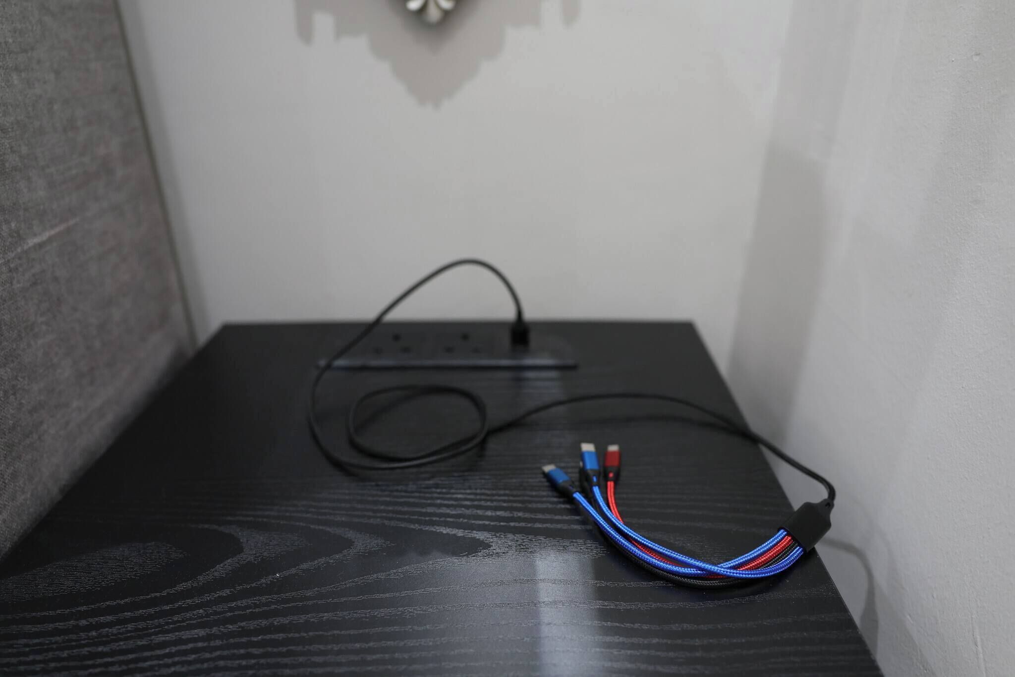 A black wooden surface with a power strip and a multicolored cable.