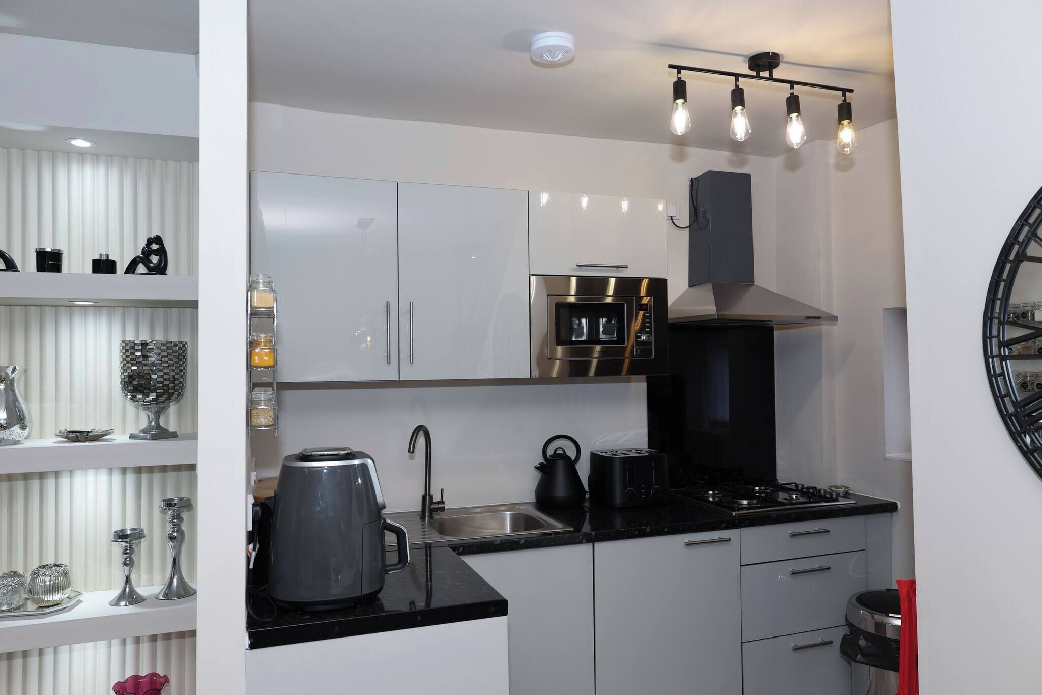 Een moderne keuken met witte kasten, een zwart aanrecht, een ingebouwde oven, een waterkoker en een koffiezetapparaat.