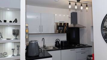 Een moderne keuken met witte kasten, een zwart aanrecht, een ingebouwde oven, een waterkoker en een koffiezetapparaat.