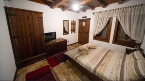 Un dormitorio con cama de madera, armario, televisor y ventana con cortinas.