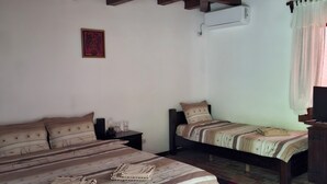 Un dormitorio con dos camas, techo de madera, aire acondicionado de pared, un cuadro enmarco y una ventana con cortinas.