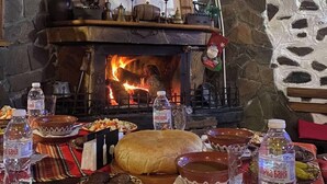 Un interior rústico con chimenea de piedra, vigas de madera y una mesa dispuesta con platos y botellas de agua tradicionales.