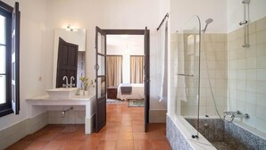 A bathroom with a sink, mirror, shower, and a doorway leading to a bedroom.