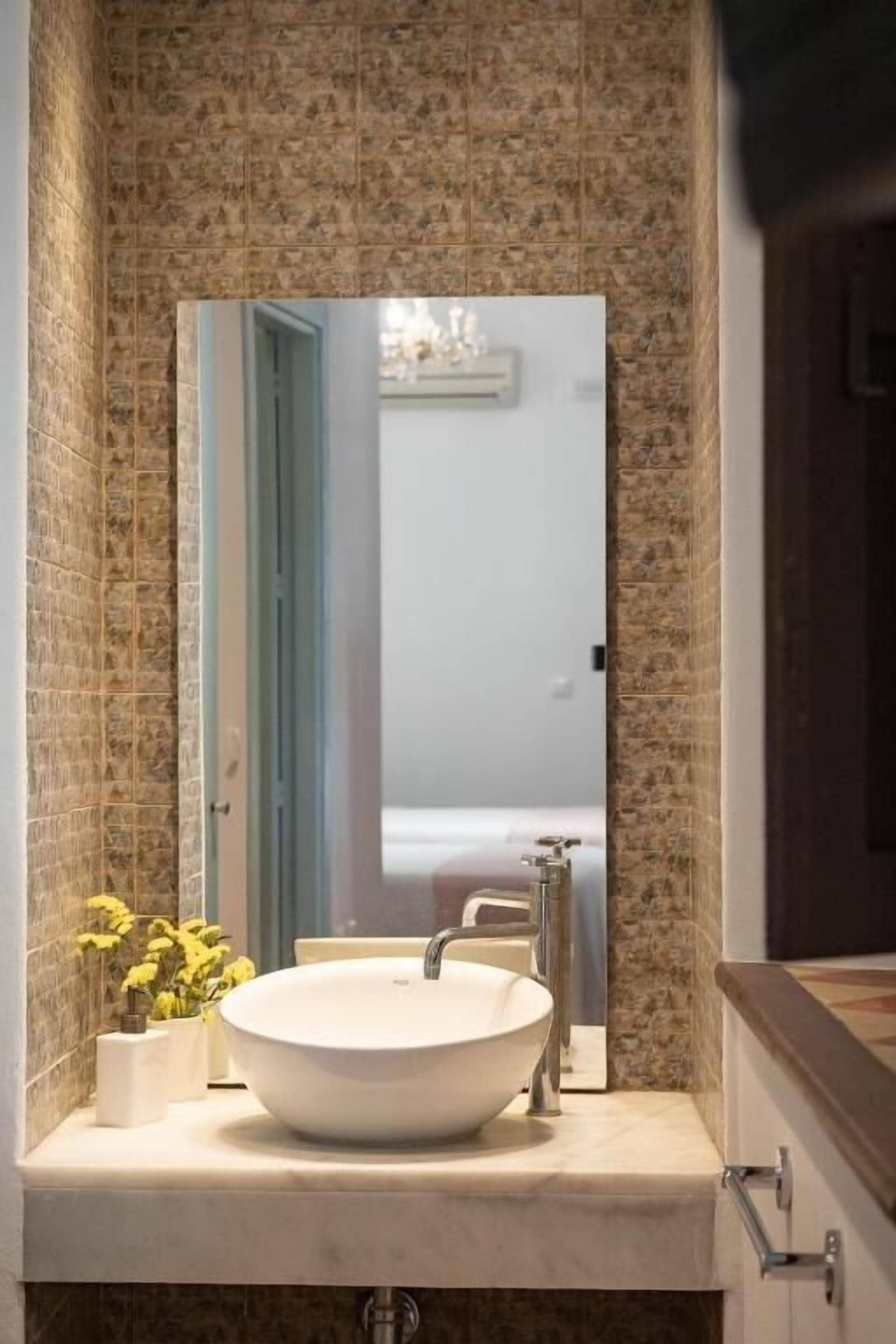 Ein Badezimmer mit einem großen weißen Waschbecken, einem Spiegel und einer Wand mit einem gemusterten Fliesendesign.