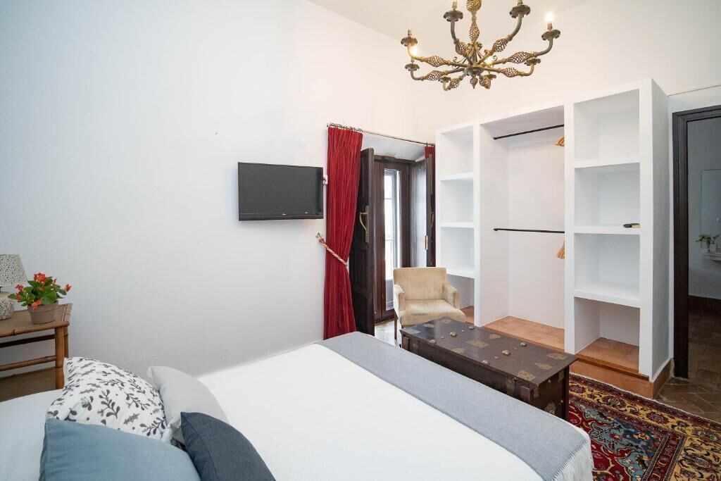 Een slaapkamer met een bed, een televisie, een stoel, een kledingkast en een kroonluchter.