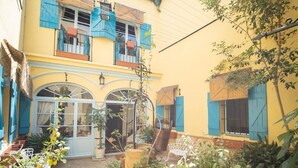 A courtyard with a yellow building, blue shutters, and potted plants.