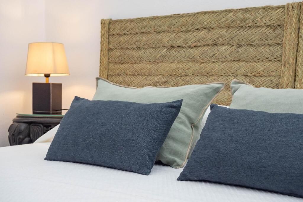 Una cama con cabecera trenzada, una lámpara de noche y dos almohadas.
