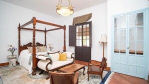 A four-poster bed, a wooden table, a chair, a lamp, and a blue door.