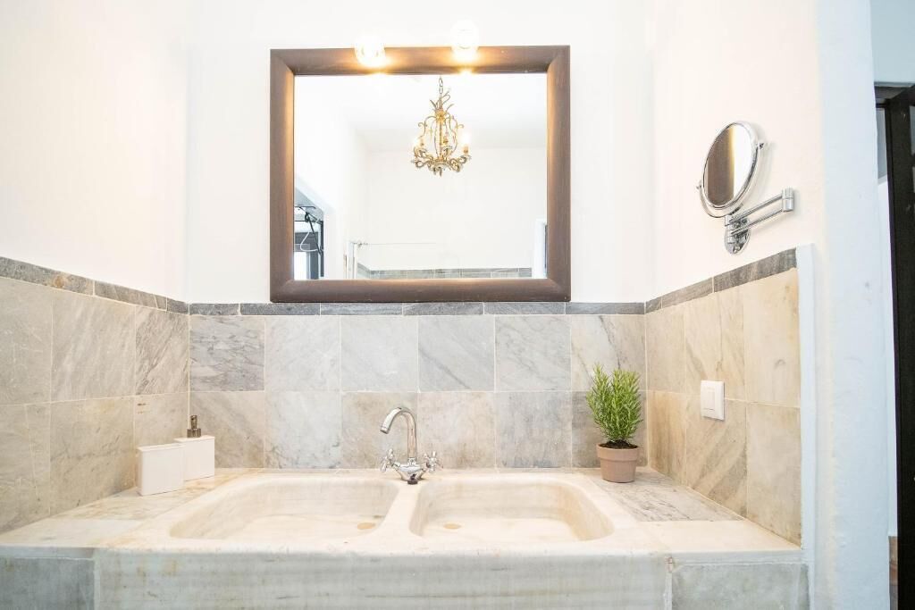 Une salle de bain avec un double lavabo, un miroir, un lustre et une plante en pot.