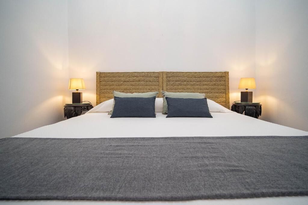 A bed with a woven headboard, two bedside lamps, and a grey throw blanket.