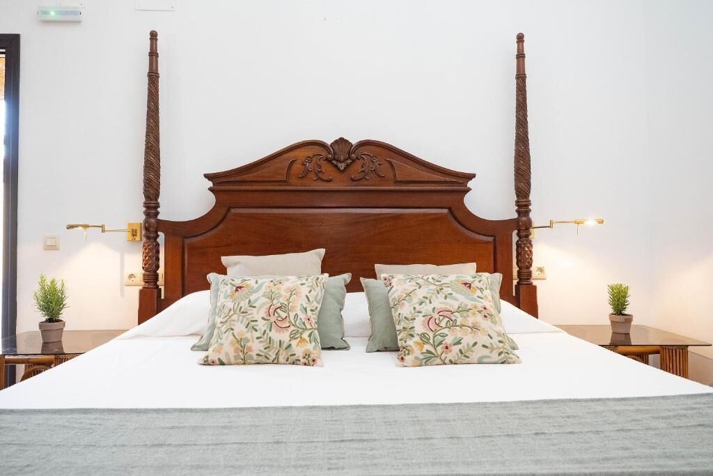 Een bed met houten hoofdbord, twee nachtkastjes met lampen en kussens met bloemenprint.