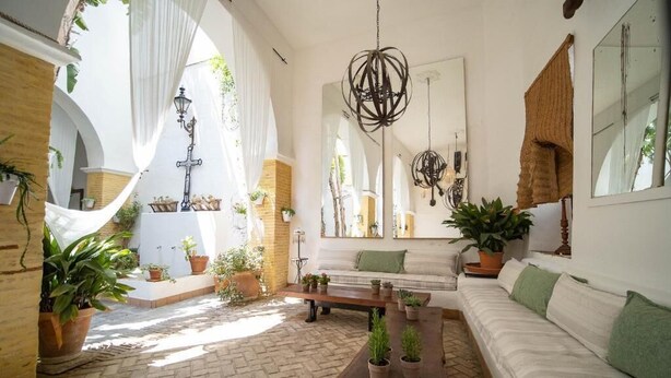 An interior with a brick floor, white walls, a wooden bench, a sofa, and potted plants.