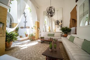 Interior com chão de tijolos, paredes brancas, um banco de madeira, um sofá e plantas em vasos.