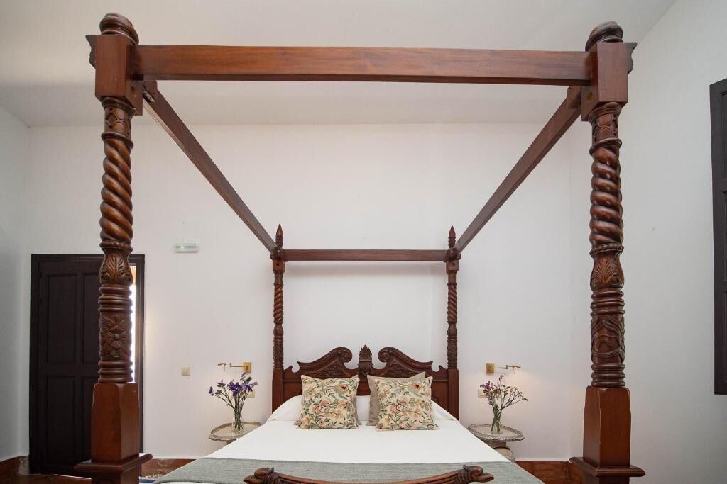 Ein Himmelbett mit Holzrahmen und einer grünen Bettdecke.