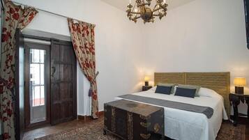 Quarto com uma cama grande, uma cômoda, um lustre e uma porta com cortinas.