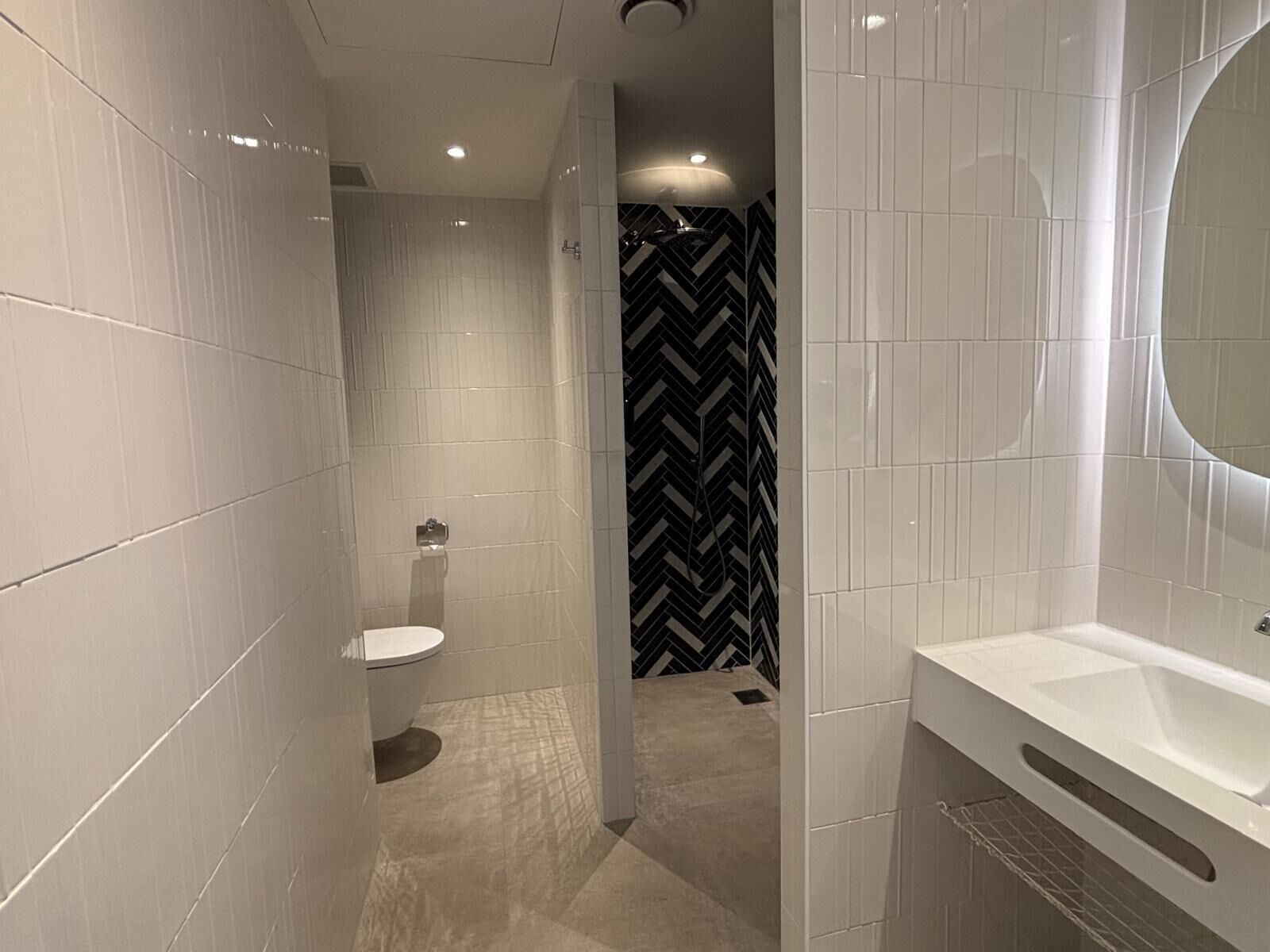 Un baño moderno con baldosas blancas, un lavamanos blanco y una pared con estampado blanco y negro.
