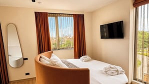 Una cama redonda con cabecera, un televisor de pantalla plana en la pared y vistas al verdor exterior.