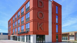 Un edificio de varios pisos con un llamativo letrero 'DOK' en la fachada, con grandes ventanales y un diseño arquitectónico moderno.