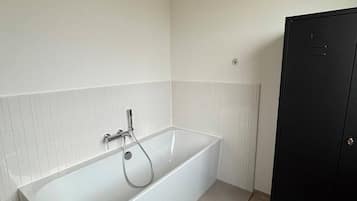 Ein modernes Badezimmer mit einer weißen Badewanne, einem schwarzen Kleiderschrank und einer Lüftung an der Wand.