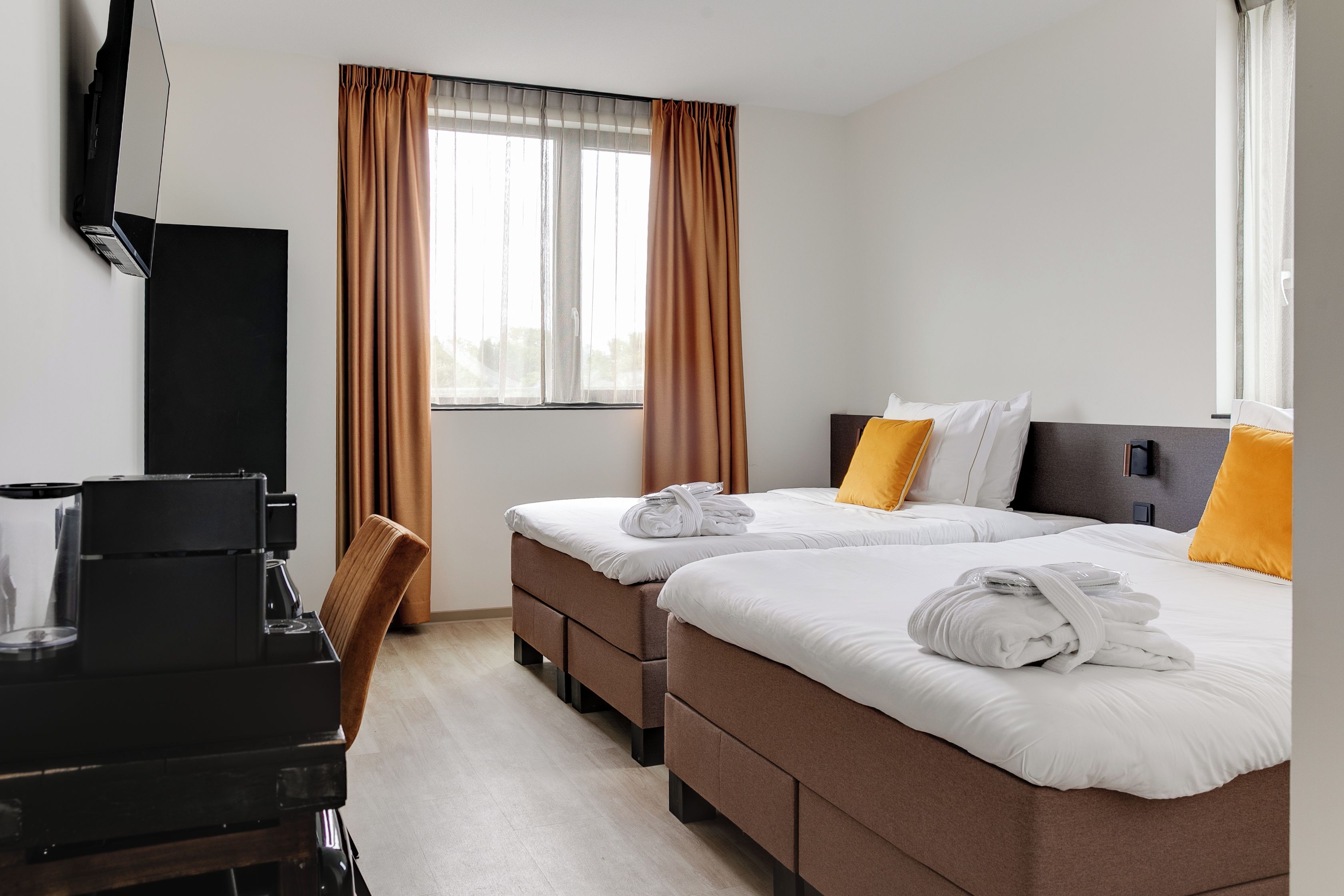 A hotel room with two beds, a desk, and a coffee machine.