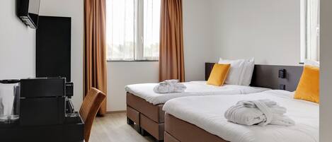 A hotel room with two beds, a desk, and a coffee machine.