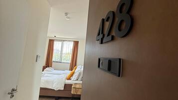 Ein Hotelzimmer mit einem Bett, einem Nachttisch, einem an der Wand befestigten Lichtschalter und einer Tür mit Griff.