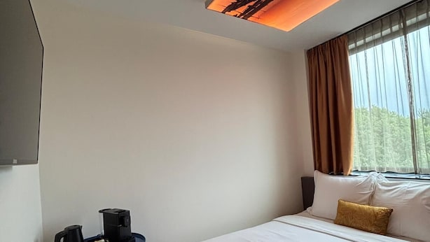 Habitación de hotel con cama, cafetera, dispensador de agua azul y ventana con cortinas.