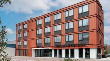 A modern hotel building with a red facade, multiple windows, and a clear sky.