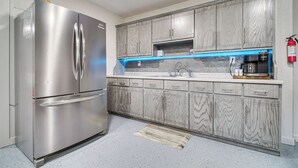 Una cocina con un refrigerador de acero inoxidable, gabinetes con diseño de mármol, una salpicadera iluminada en azul y una cafetera.