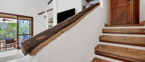 Una escalera de madera con barandilla, que lleva a una habitación con un ventanal y vistas a árboles.