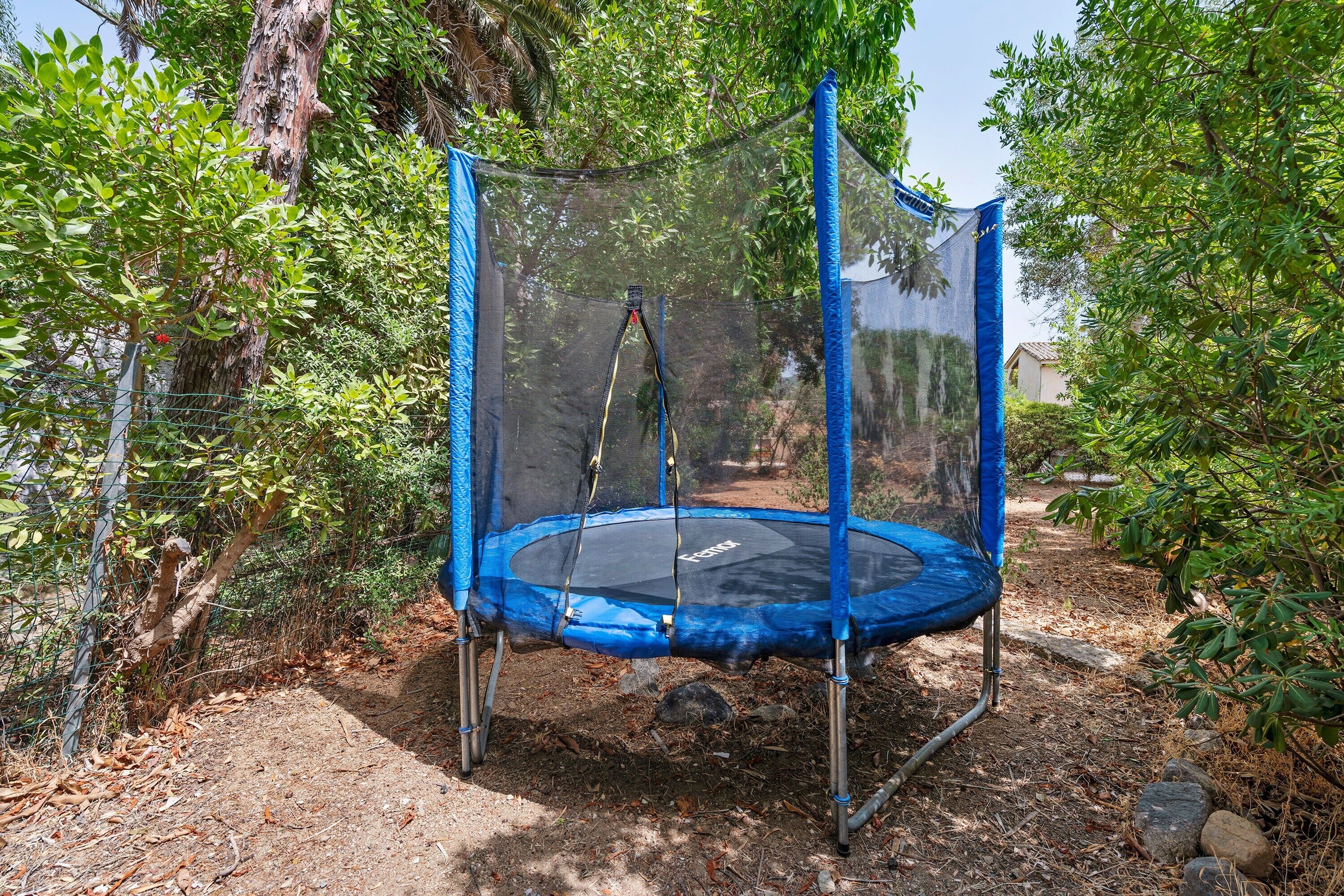 Un trampoline doté d’un filet de protection, entouré d’arbres et d’une clôture.