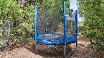 Un trampoline doté d’un filet de protection, entouré d’arbres et d’une clôture.